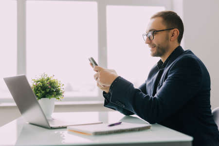 Manager in formal wear holding mobile phone in hands, thinking of business opportunity alone in...