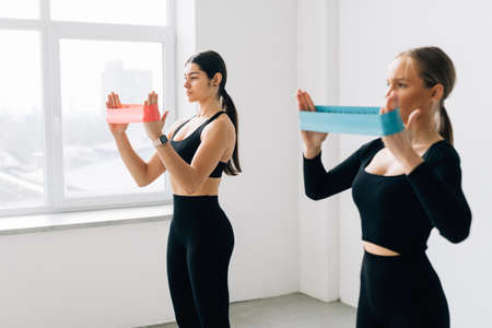 Two beautiful young adult females using resistance bands at the gym