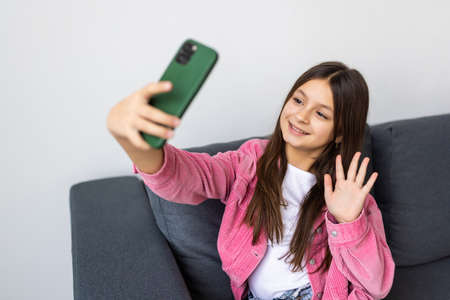 Portrait of attractive cheerful girl influencer blogger sitting on sofa taking selfie video...