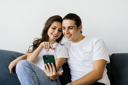 Young couple sitting on a couch at home looking at mobile phone