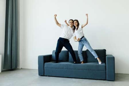 Picture of a cheerful couple jumping and dancing together on the couch. Shot at homeの写真素材