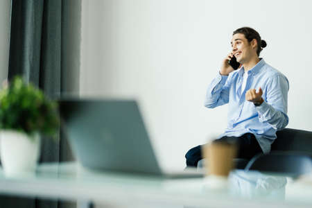 Portrait of handsome young male in glasses sitting at office desk with laptop computer and talking...