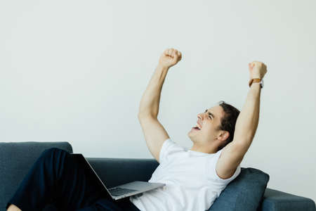 Excited man using laptop computer while sitting on a sofa at home