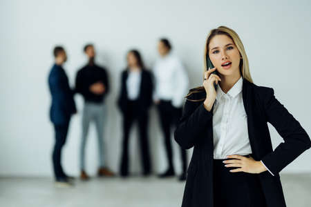 Businesswoman on the phone smiling at camera with team behind her in the officeの写真素材
