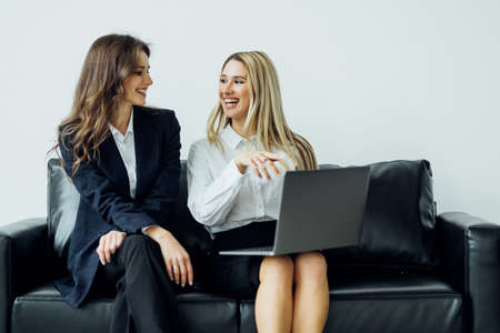 Two women have a business discussion on a couch in an office with a laptop computer.の写真素材
