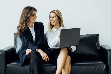 Two women have a business discussion on a couch in an office with a laptop computer.の写真素材