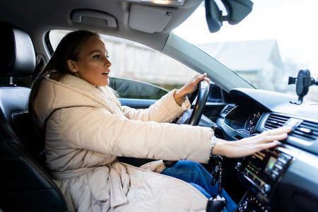 Young woman smiling and pushing buttons while driving a car