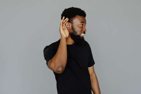 Close up portrait of african man holding hand near ear and trying to hear the information isolated on gray backgroundの写真素材