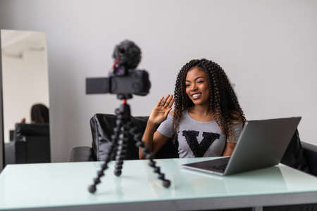 Happy girl at home speaking in front of camera for vlog. Young black woman working as blogger,...