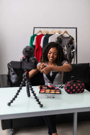 happy young african american woman streaming a beauty vlog from home, online content creator applying a makeup onの写真素材