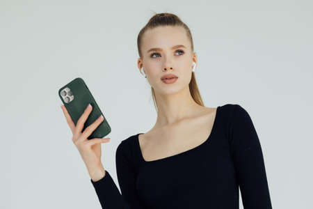 Portrait of a fitness woman listening to music with earphones while standing and using mobile phone...
