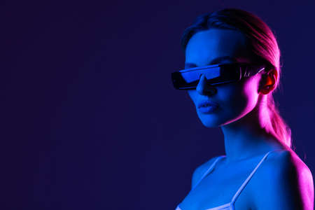 Young model posing in a studio in a trendy neon light. Woman in sunglasses and hoodie with colorful light effects.の写真素材