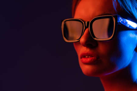 Young woman beauty face wear stylish eyewear glasses look at camera in neon light purple blue backgroundの写真素材
