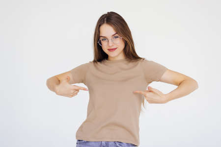 Portrait of caucasian woman with short brown hair in basic t-shirt rejoicing and pointing fingers at herself isolated over white backgroundの写真素材