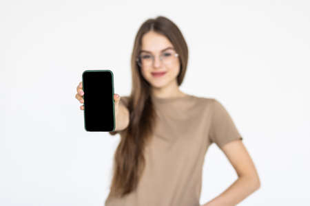 Happy beautiful young woman with long curly hair holding blank screen mobile phone and pointing...