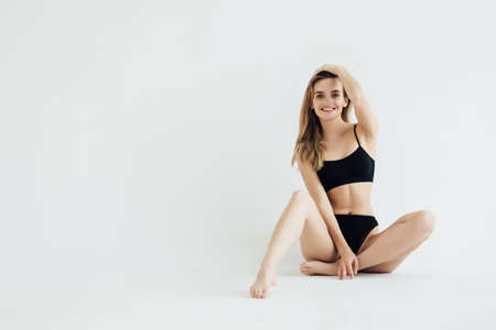 young beautiful woman with perfect body in black underwear sitting on floor isolated on white backgroundの写真素材