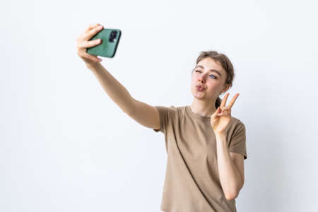 Self-portrait of pretty laughing dreaming girl in striped t-shirt showing v-sign near her eyesの写真素材