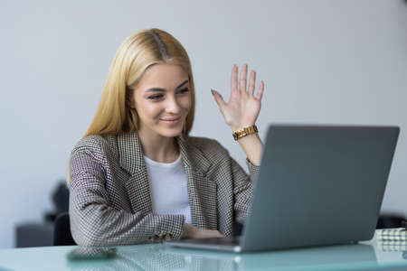 View over businesswoman shoulder sit at workplace desk looks at pc screen during group videocall...