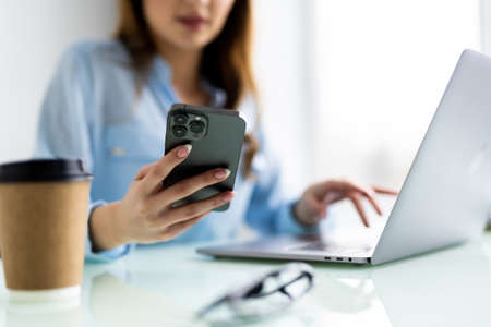 Woman hand uses a mobile phone and works in a laptop at offices.の写真素材