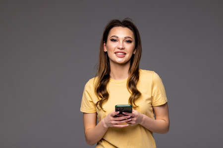 Portrait of a young woman using mobile phone while standing over gray backgroundの写真素材