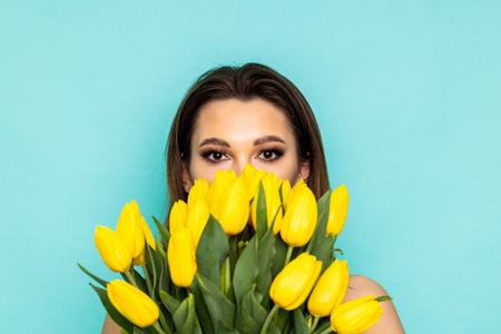 Portrait of a cheerful young girl in dress holding yellow tulips bouquet isolated over blue backgroundの写真素材