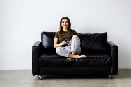 Happy girl texting on a mobile phone resting on a couch at homeの写真素材