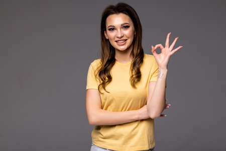 Beautiful young woman showing Ok sign isolated on gray wall background