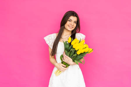 spring flowers. Young gorgeous girl in a bright pink dress is looking in the camera with a big smile, holding a bunch of tulips in her hands.の写真素材