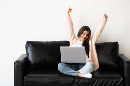 Young woman sit on couch at home triumph receive pleasant email or read good news on laptop onlineの写真素材