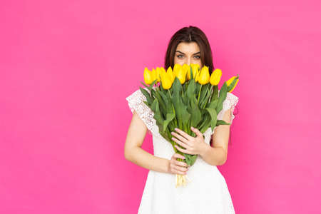 Portrait of a beautiful young girl in dress holding big bouquet tulips isolated over pink backgroundの写真素材