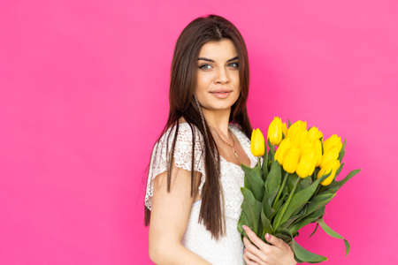 spring flowers. Young gorgeous girl in a bright pink dress is looking in the camera with a big smile, holding a bunch of tulips in her hands.の写真素材
