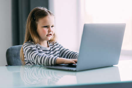 Cute little girl smiling and looking at laptop