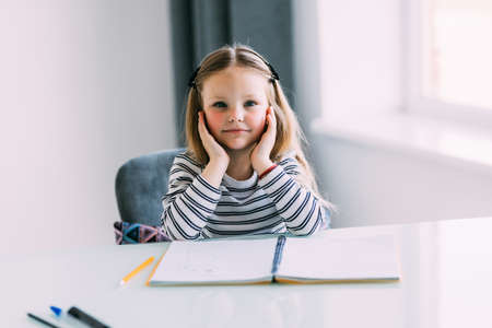 Unhappy little Caucasian girl child sit at table at home feel lazy unmotivated doing homework...