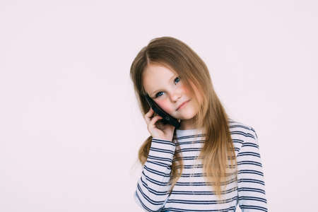 The little girl phones on the white wall backgroundの写真素材