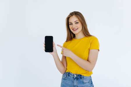 Happy young woman holding blank screen mobile phone and pointing finger over white background