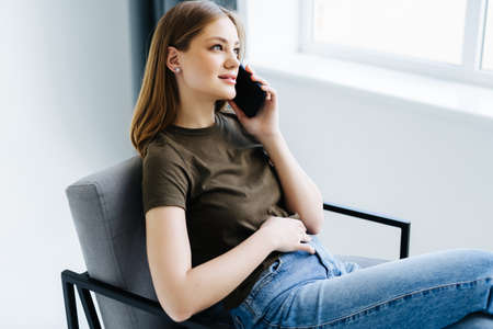 Portrait of a young professional girl sitting smiling at home using a smartphone mobile phone to...