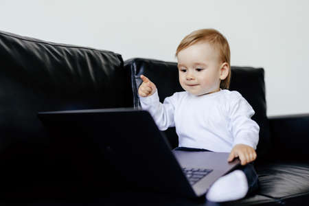 Picture of little cute boy using laptop computer while lying on sofa at home. Look at laptop.