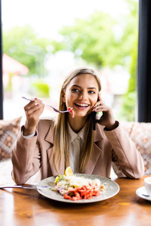 Pretty woman eating salad in a cafe and talking on the phoneの写真素材