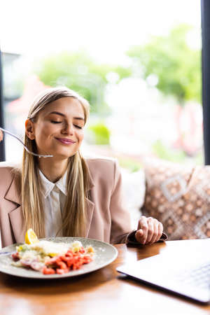 Stylish young woman eating healthy salad on a restaurant terrace, feeling happy on a summer dayの写真素材