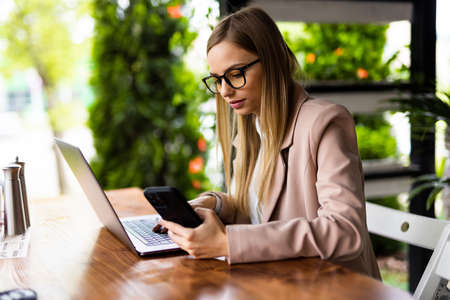 Portrait image of a young woman holding and using mobile phone and laptop computer in cafeの写真素材