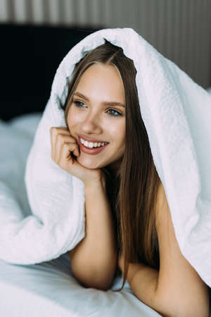 Smiling young woman under a duvet in her bedroomの写真素材