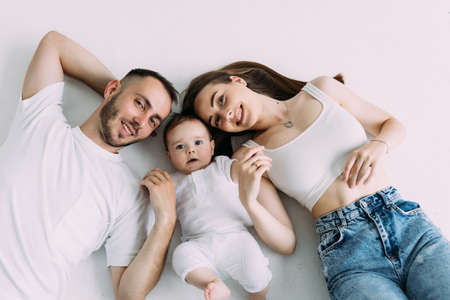 Young parents lying in bed, playing and looking at their cute little baby from above.