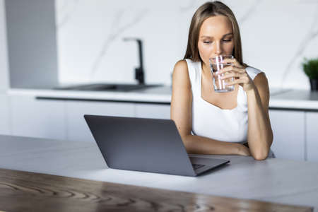 Many stuff to do today in home office. Woman sitting in kitchen table, looking at laptop computer screen. Female entrepreneur working sitting at a desk typing on her laptop computer in a home officeの写真素材