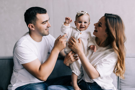 Photo of young cheerful family happy positive smile mommy daddy daughter laugh look each other sit sofa indoorsの写真素材