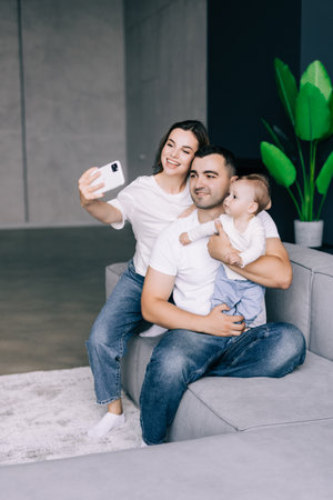 family, parenthood and people concept - happy mother and father with baby taking selfie at home