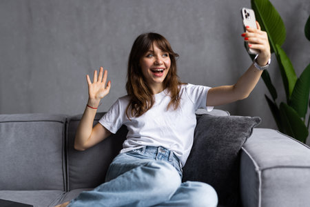 Shot of a happy young woman taking selfie with her cellphone while sitting at living room.の写真素材
