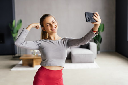 Young smiling sporty athletic fitness trainer instructor woman doing exercises do selfie shot on mobile cell phone sit on mat floor at home gym indoorの写真素材