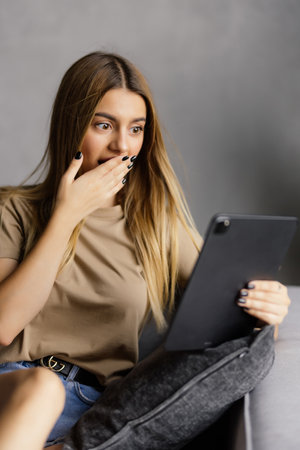 Surprised woman with tablet lying on couchの写真素材