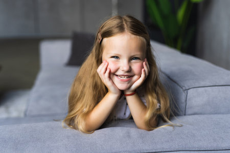 Little girl having fun at home. Happy smile on the child's face. Little girl lying on her stomach on the couchの写真素材