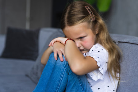 Depressed young girl hugging her knees and feeling like crying alone at home. Little kid lonely at homeの写真素材
